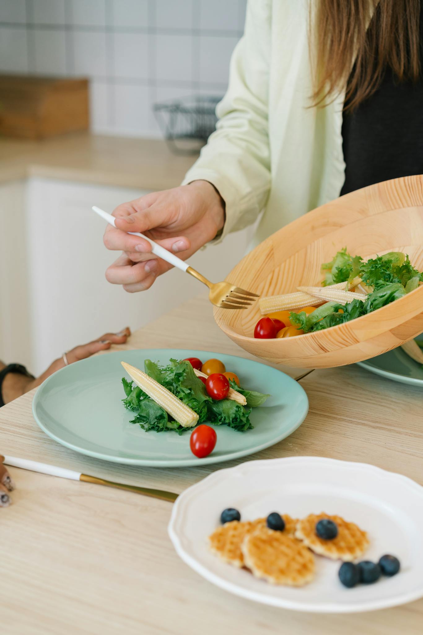 Person serving a fresh salad with baby corn, tomatoes, and greens for a healthy meal.